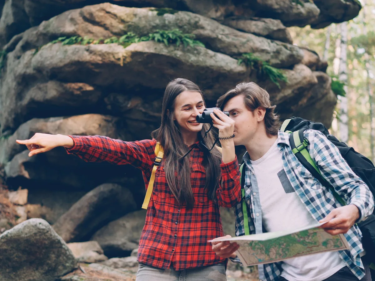 Two spotters checking a paper map and binoculars together on a woodland trail